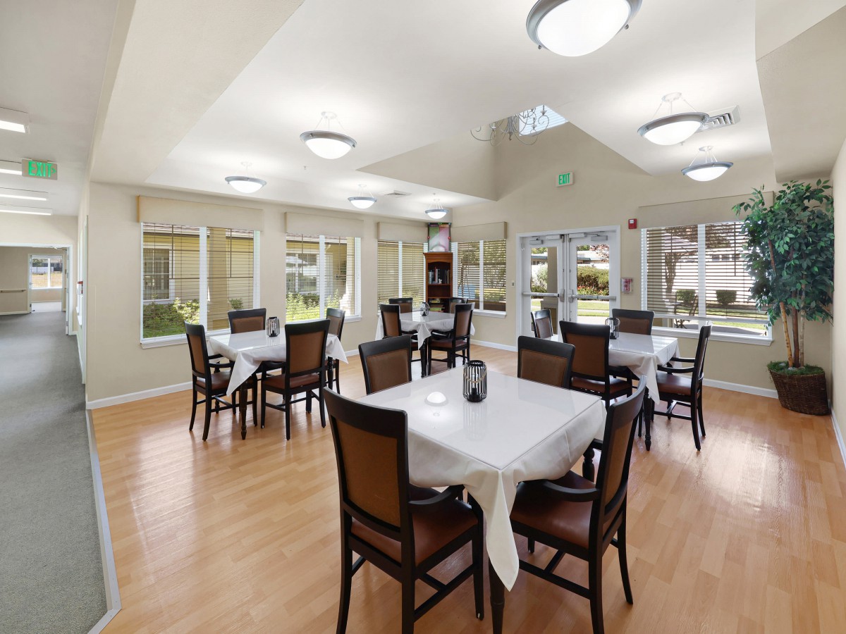 A spacious dining room with multiple tables and chairs, featuring large windows and modern lighting.