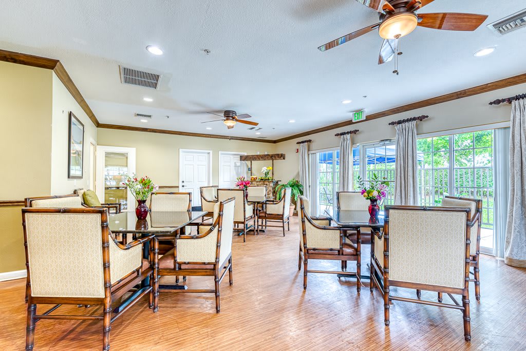 A well-lit dining area with elegantly arranged tables and chairs, featuring ceiling fans and large windows.