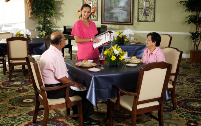 A waiter presenting a menu to two seated customers in a restaurant.