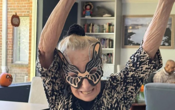 A joyful person wearing a playful mask and raising their arms, celebrating indoors.