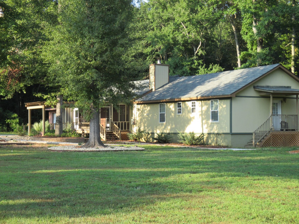 A cozy house with a large yard surrounded by trees.