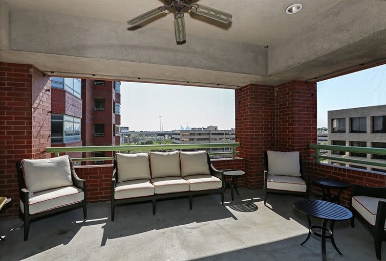 A spacious outdoor balcony with comfortable seating and a ceiling fan, surrounded by brick walls.