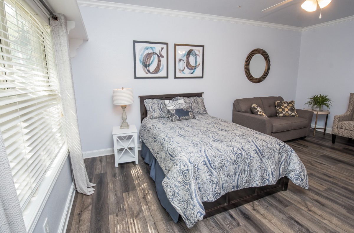 A cozy bedroom featuring a bed with patterned bedding, a sofa, wood flooring, and decorative elements.