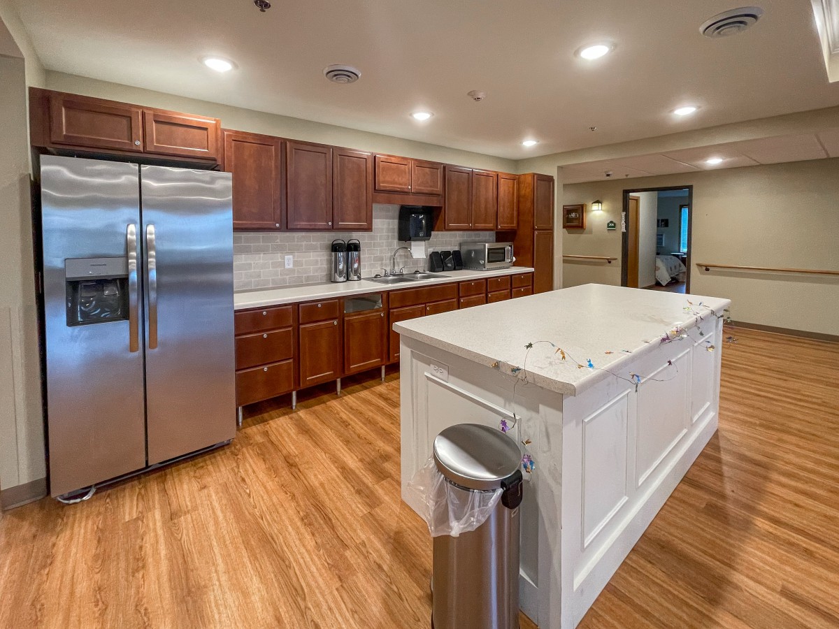 A modern kitchen with wooden flooring, featuring a large island counter and stainless steel appliances.