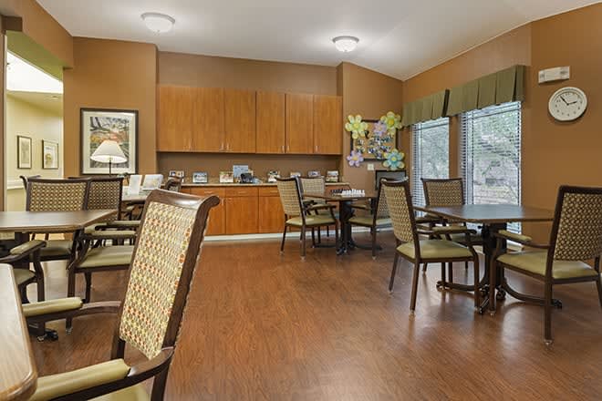 A spacious and well-lit dining area with wooden floors, arranged with tables and chairs for guests.
