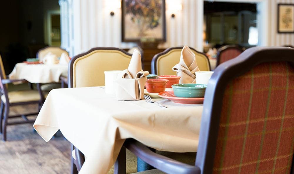 A neatly set dining table in a restaurant with napkins, plates, and chairs.