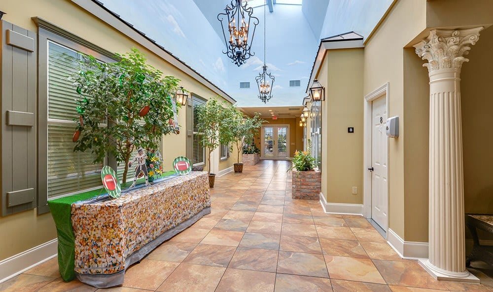 A welcoming indoor hallway with chandeliers, plants, and a tile floor.