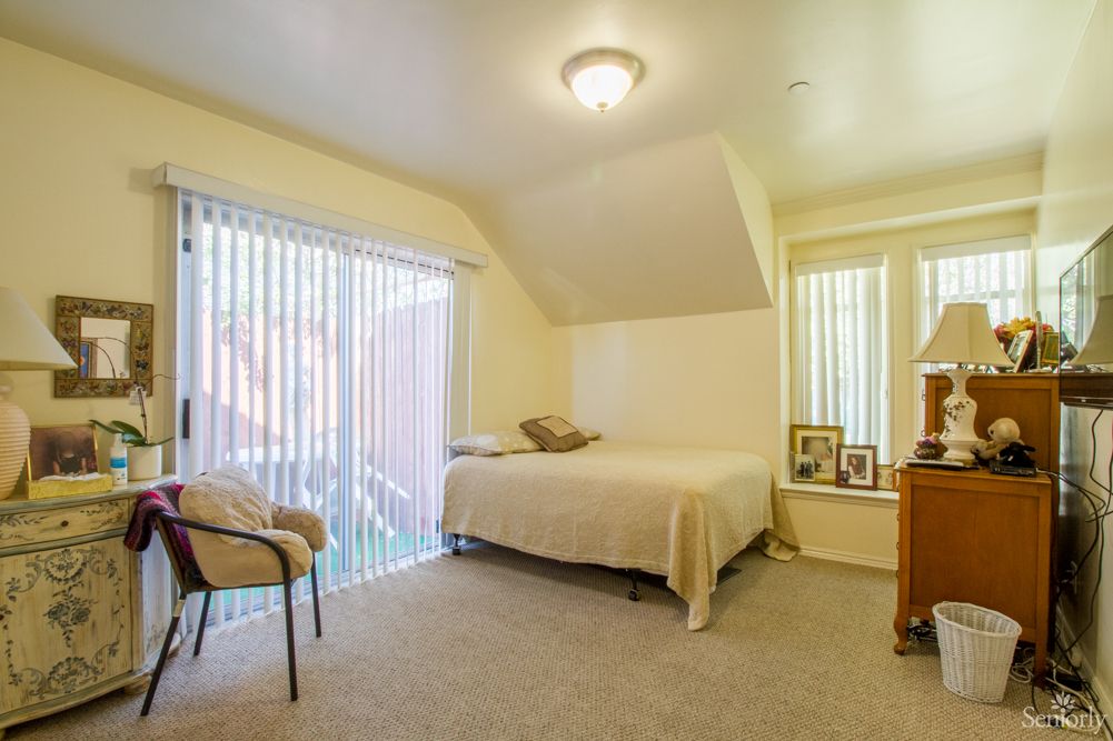 A cozy bedroom with a bed, chair, and ample natural light from large windows.