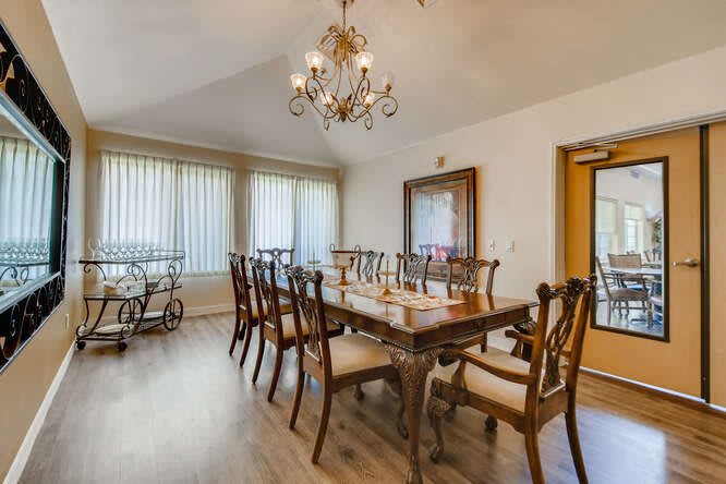 A spacious dining room featuring a large wooden table, multiple chairs, a chandelier, and natural light from tall windows.