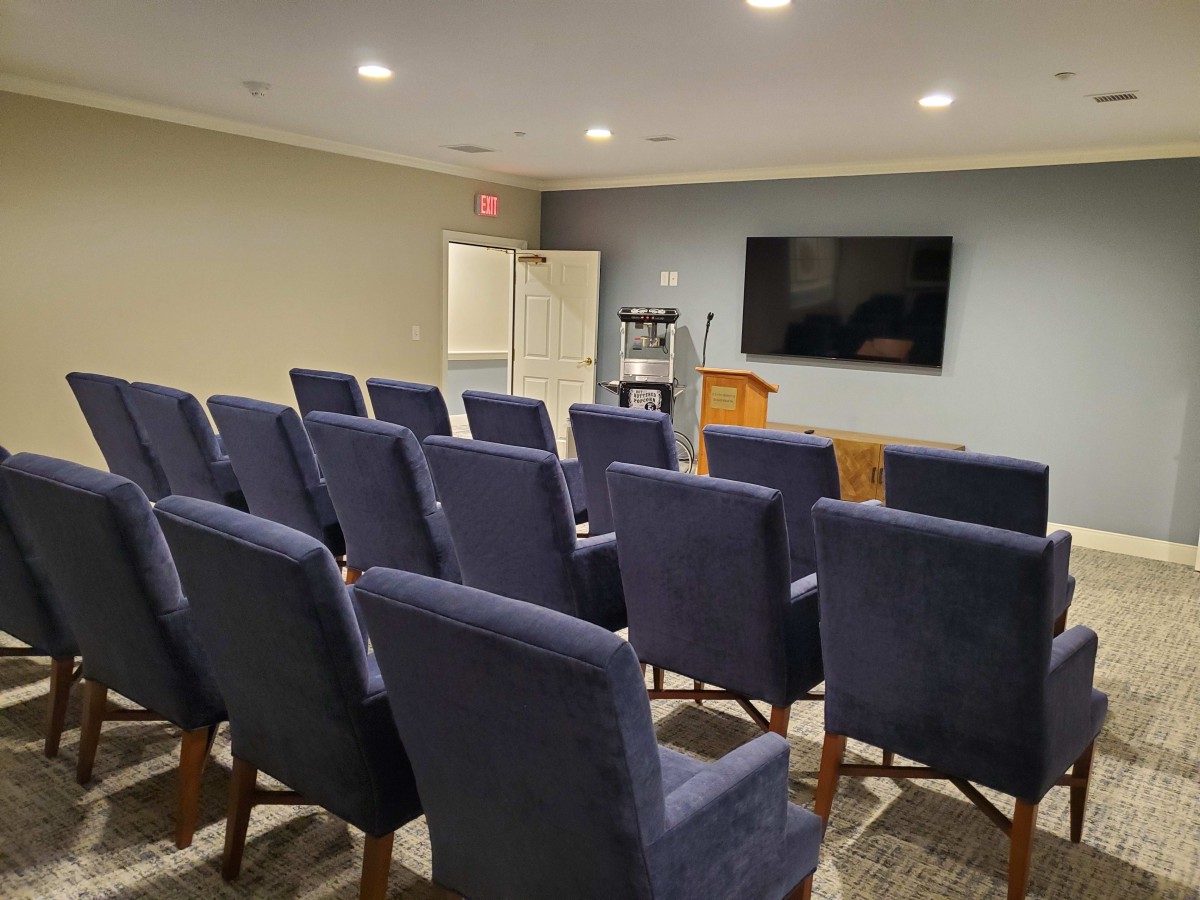 A small conference room with rows of chairs facing a podium and a television screen.