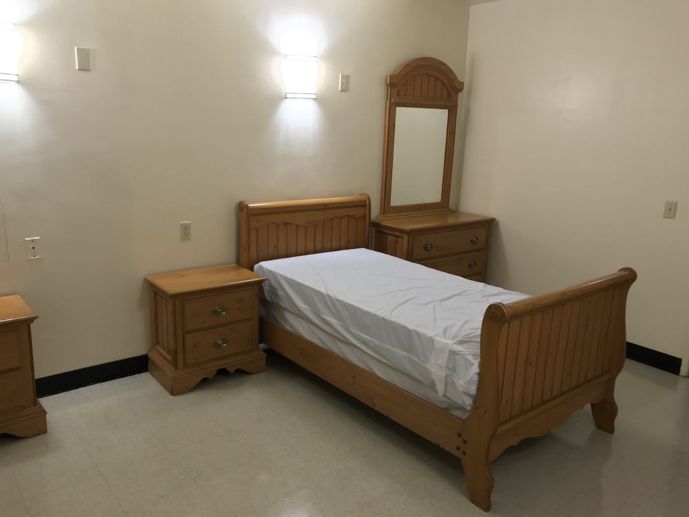 A minimalistic bedroom with a single wooden bed, nightstand, and dresser with mirror.