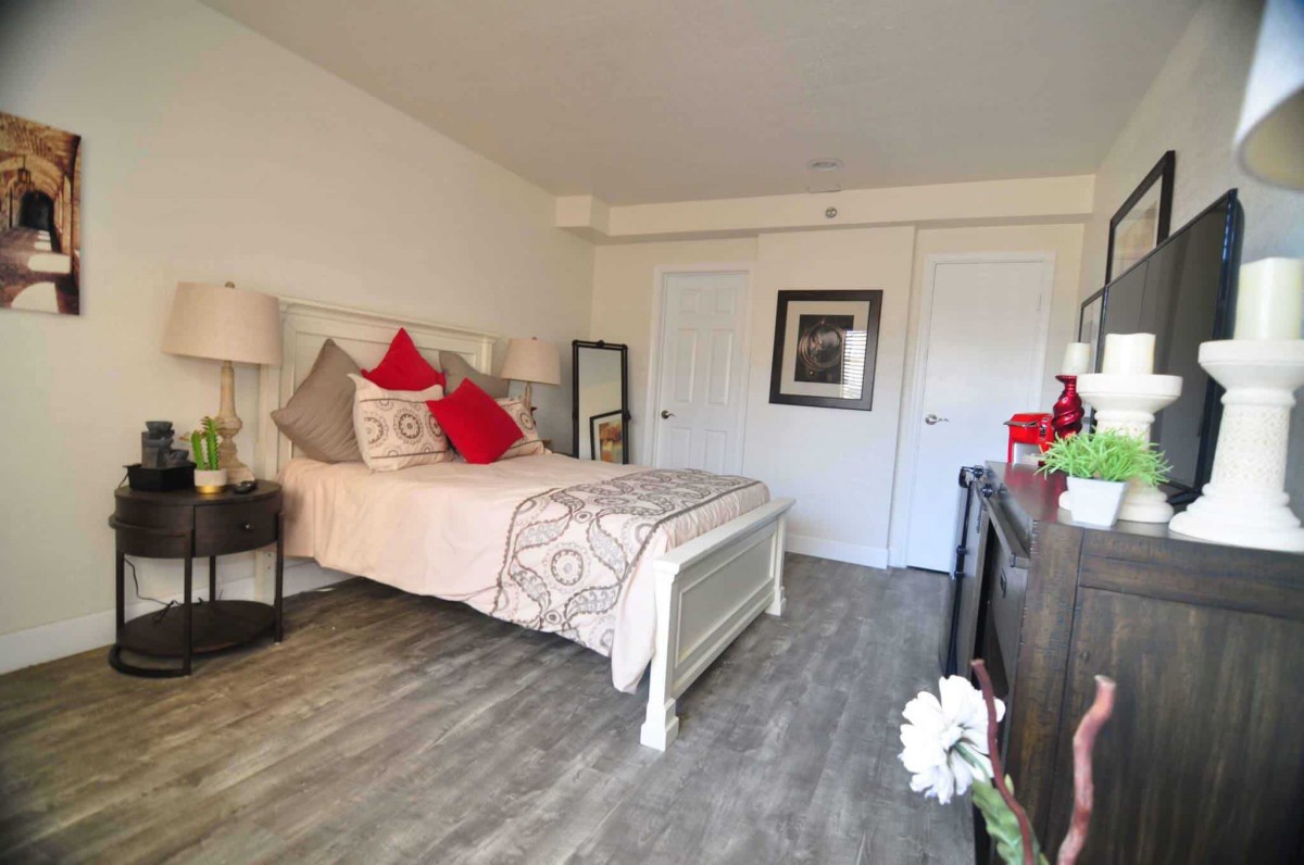 A cozy bedroom with a neatly made bed adorned with red and beige pillows, a bedside table with a lamp, and decorative elements enhancing the warm ambiance.