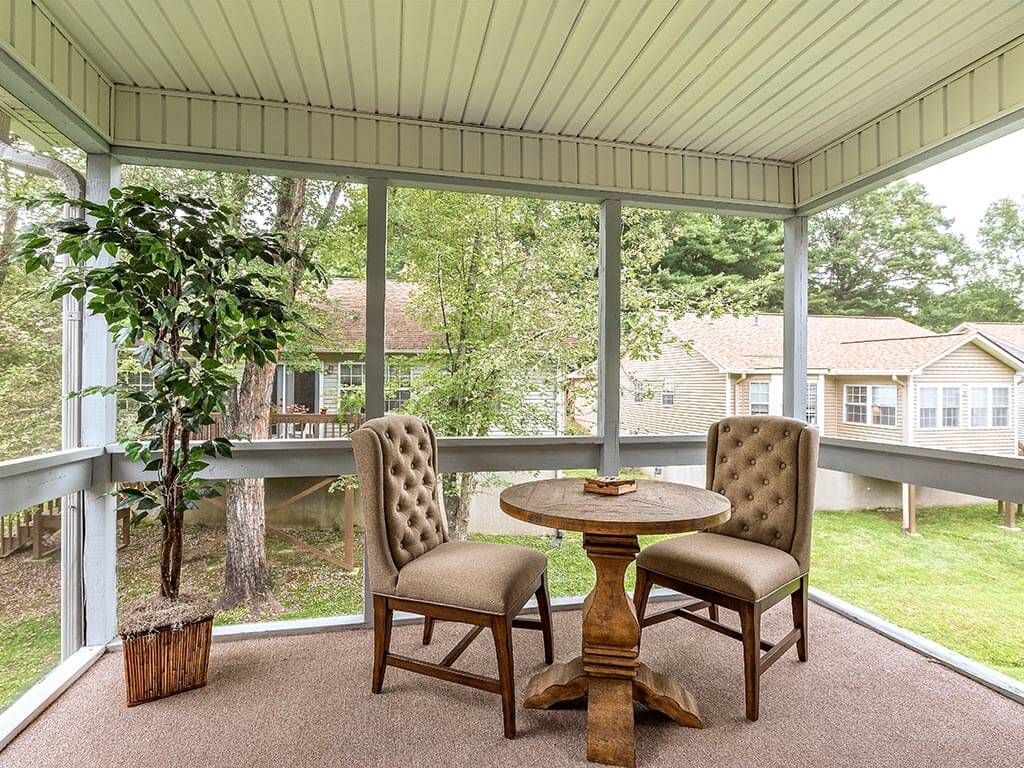 A cozy screened porch with a round table, two upholstered chairs, and an indoor plant.