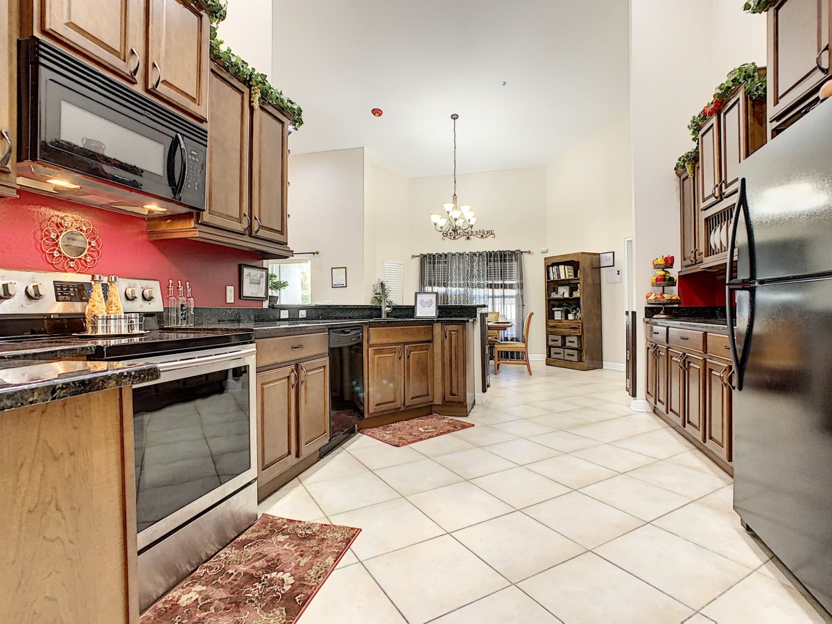 A spacious kitchen with wooden cabinets, modern appliances, and tile flooring leads into a dining area.