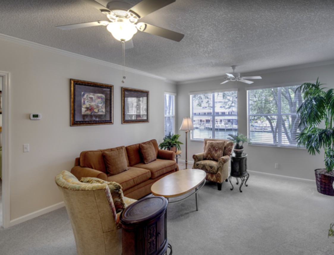 A cozy living room with a sofa, armchairs, and a coffee table illuminated by natural light through large windows.