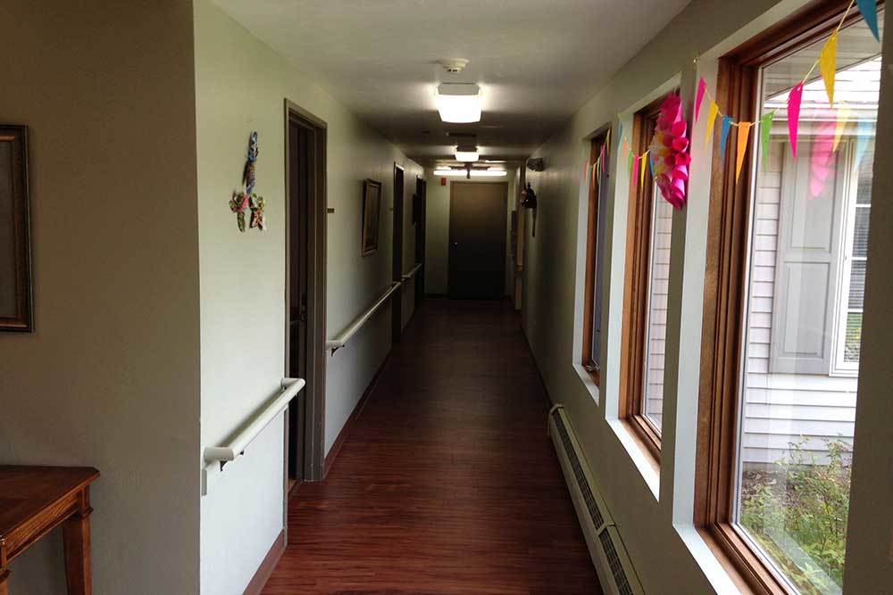 A long, well-lit hallway with wooden flooring and windows adorned with colorful decorations.