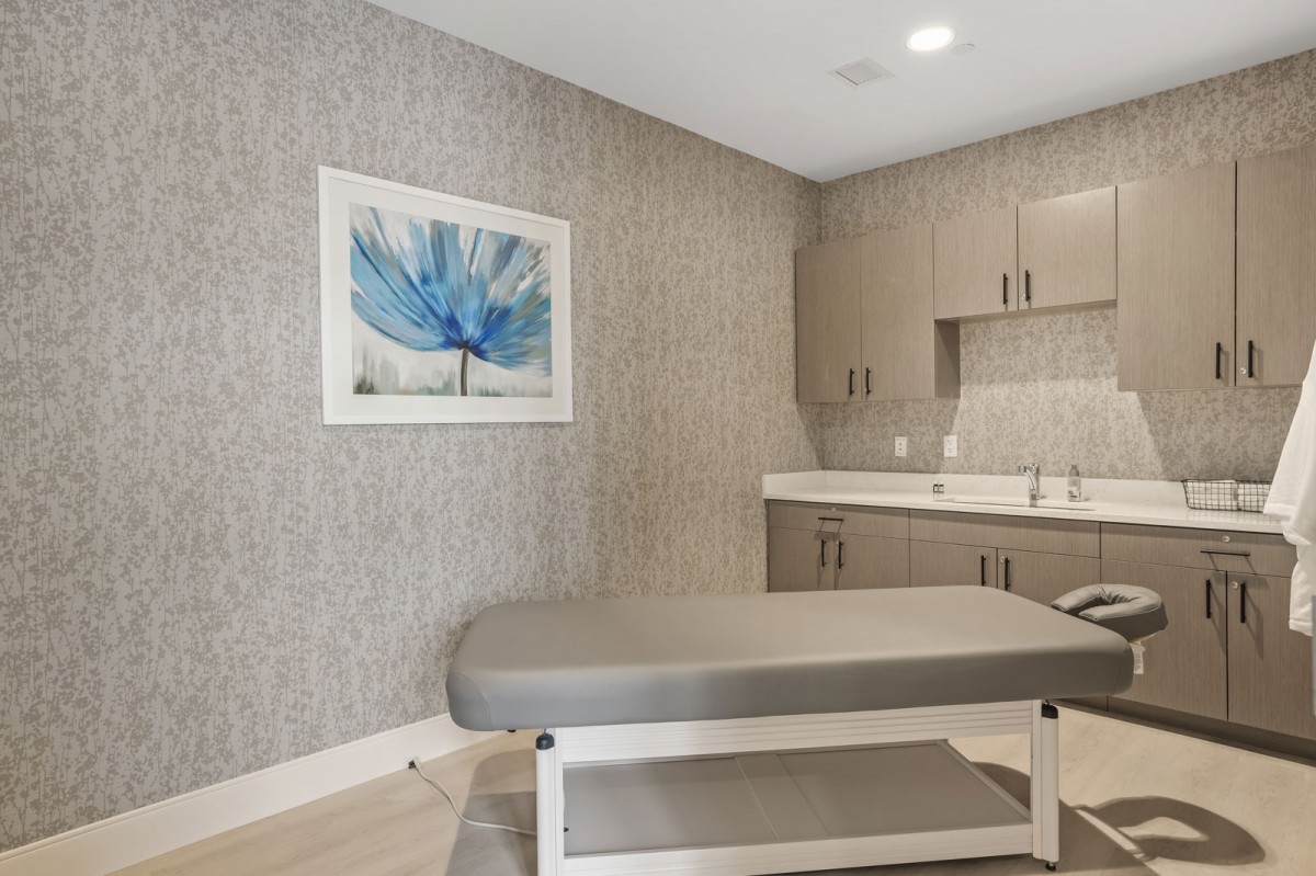 A modern therapy room featuring a treatment table, neutral tones, and artistic wall decor.