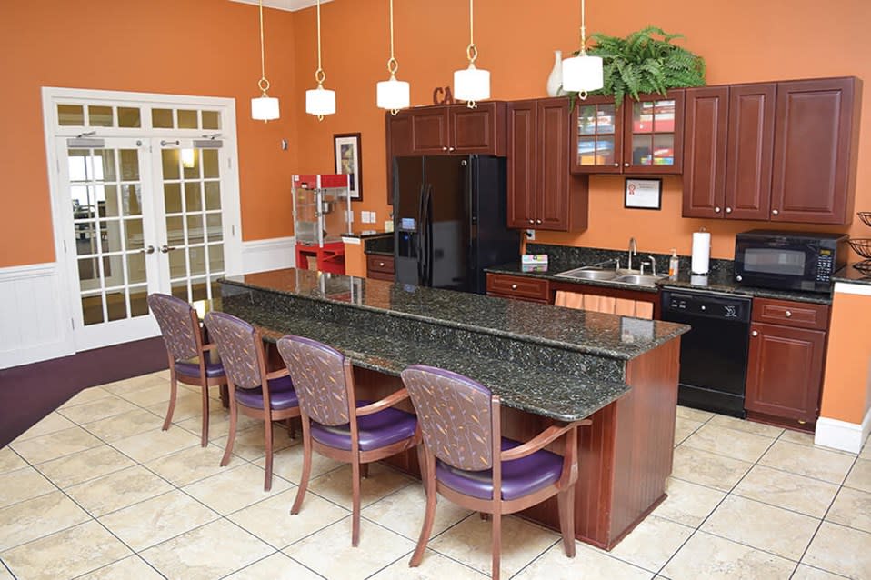 A modern kitchen with an island and bar stools, featuring granite countertops and pendant lighting.