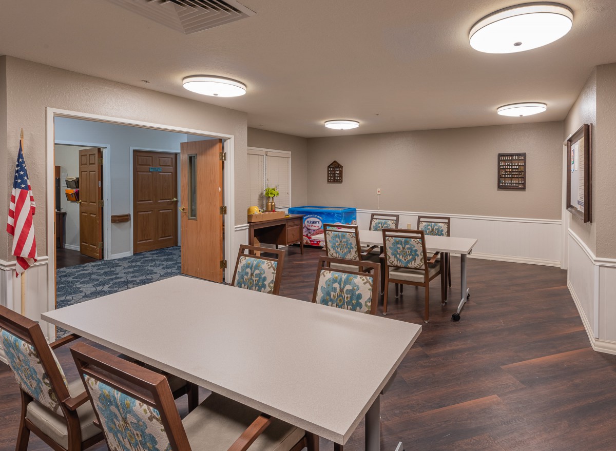 A well-lit meeting room with tables and chairs, featuring wood flooring and simple decor.