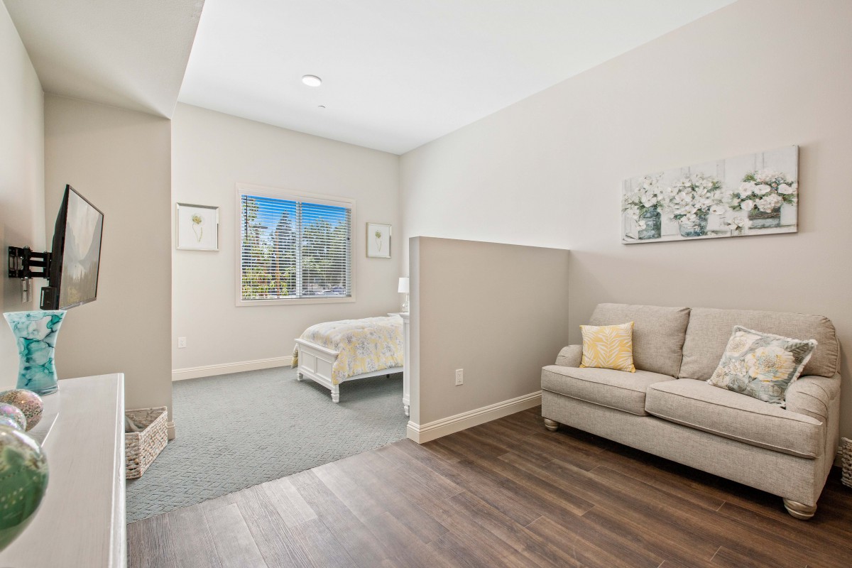 A cozy interior space featuring a small sofa and a bed with light neutral colors and wood flooring.