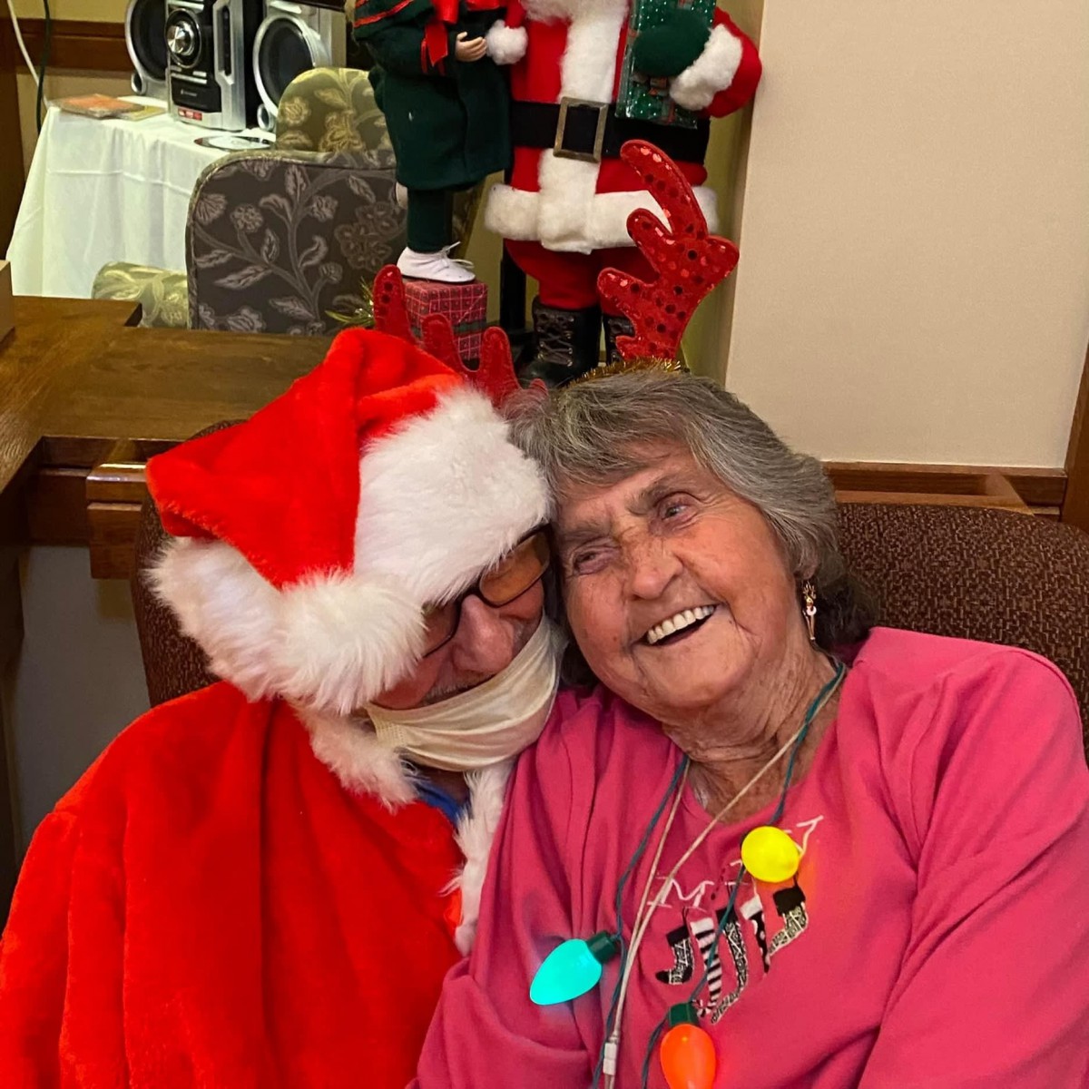 An elderly woman enjoying a festive moment with someone dressed as Santa Claus.