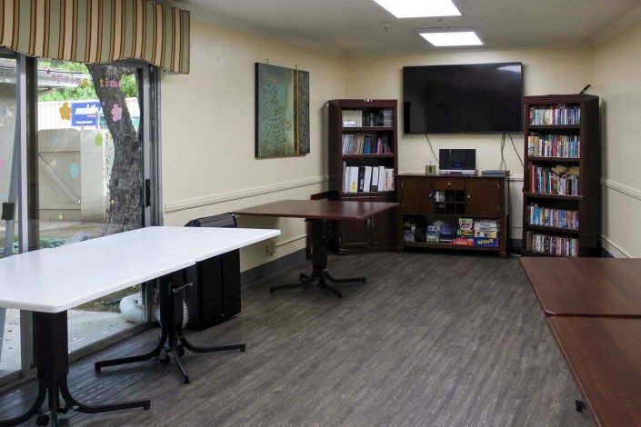 A small office meeting room with tables, a television, and a bookshelf.