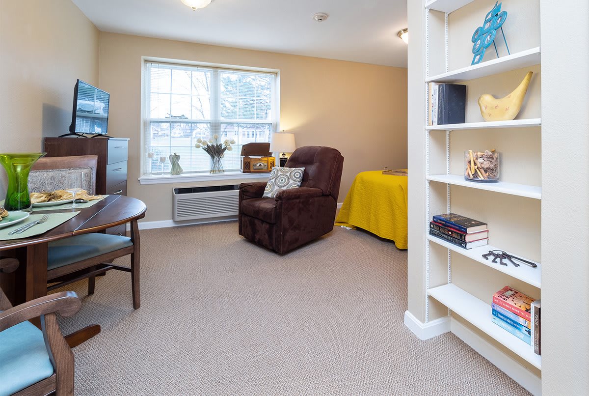 A cozy living room with a comfortable chair, bookshelf, and natural light streaming through the window.