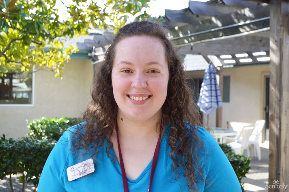 A woman smiling outdoors wearing a name badge.