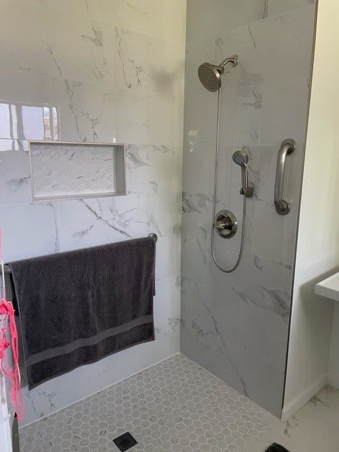 A modern bathroom shower area with marble tiles and a towel hanging on the wall.