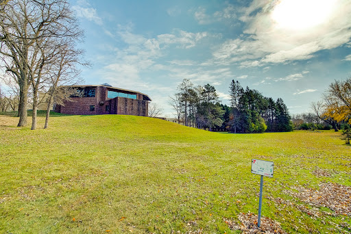 A modern building set against a lush green landscape under a partly cloudy sky.