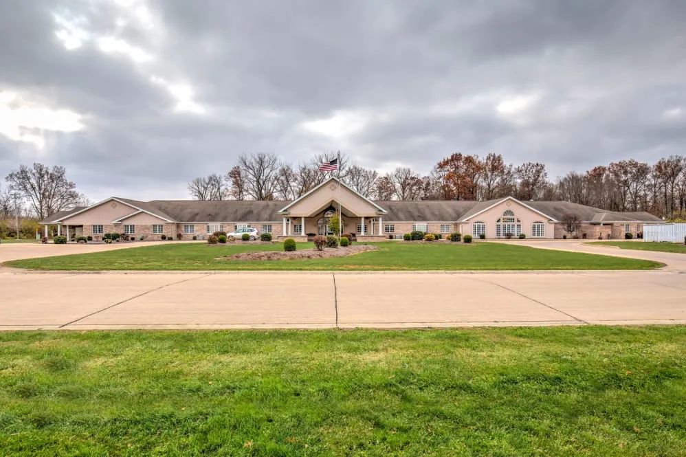 A spacious building surrounded by green grass and a cloudy sky.