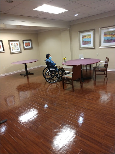 A spacious indoor area featuring a person in a wheelchair, surrounded by tables and chairs, with art on the walls.