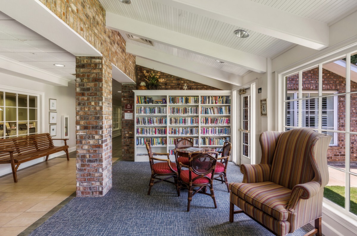 A cozy lounge area with bookshelves, chairs, and a table by a brick accent wall.