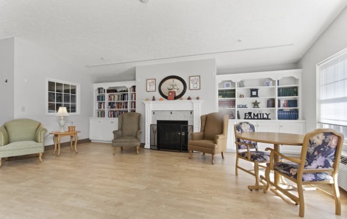 A cozy living room with a fireplace, surrounded by armchairs and built-in bookcases on a wooden floor.