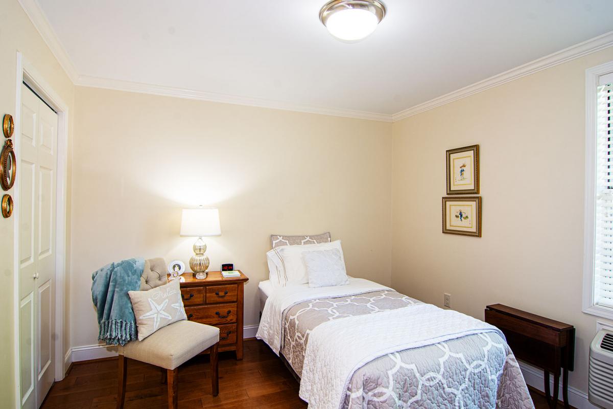 A cozy bedroom with a single bed, nightstand, lamp, and a chair.
