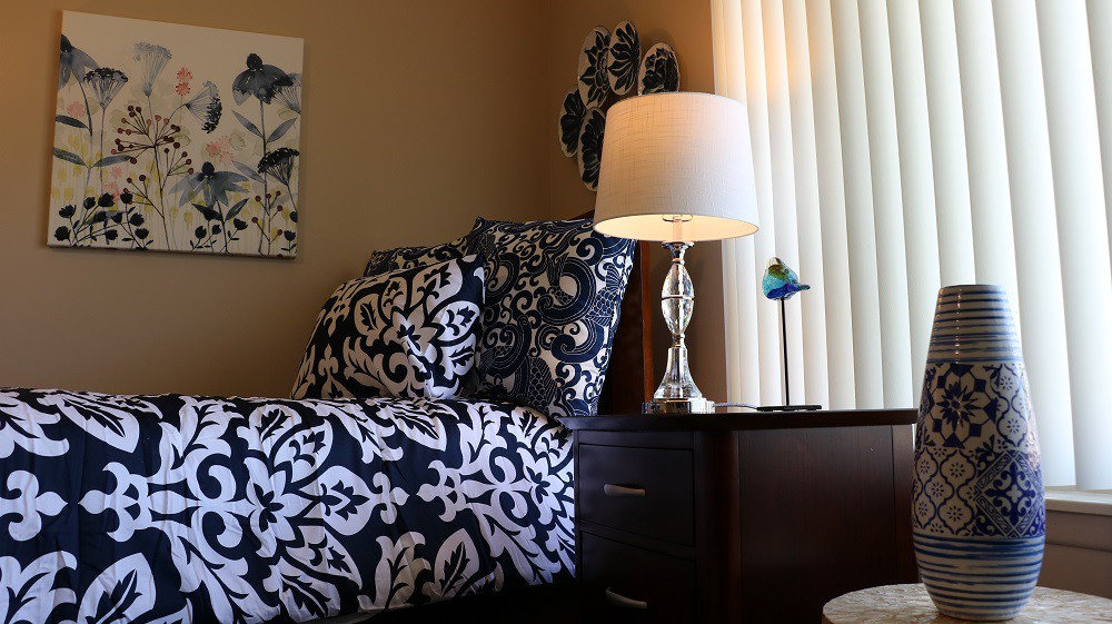 A cozy bedroom setup featuring patterned bedding and a stylish lamp on a dark wooden nightstand.