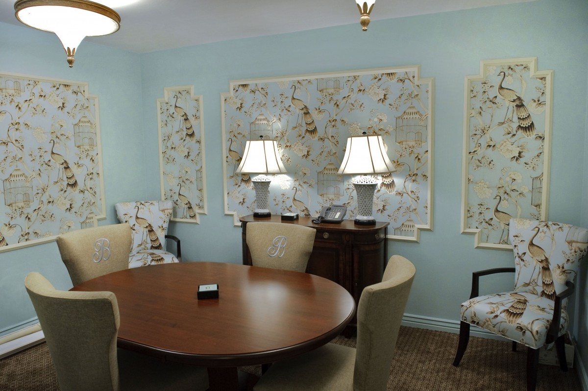 A cozy room with a round wooden table, surrounded by upholstered chairs and adorned with decorative artwork and lamps.