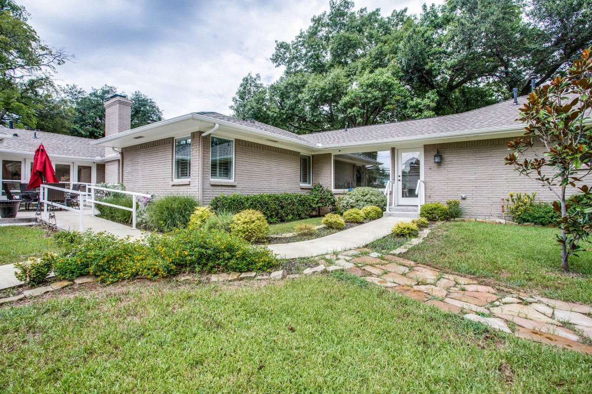 A ranch-style house with a neatly maintained front yard and pathway surrounded by greenery.