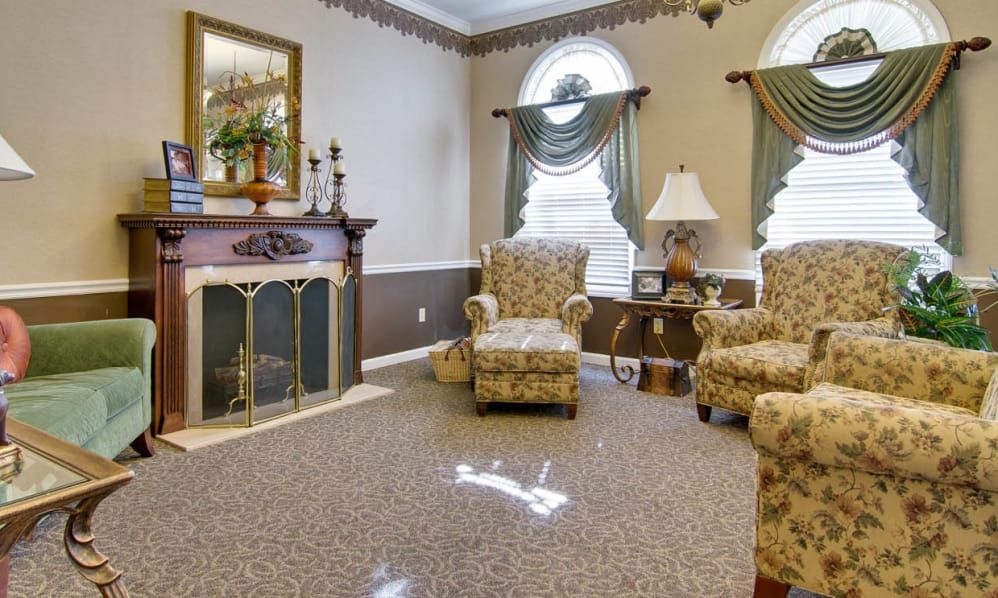 A traditional living room with patterned armchairs, a fireplace, and elegant window drapes.