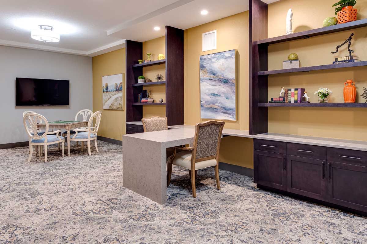 A modern office space with a large desk, built-in shelves, and a meeting area in the background.