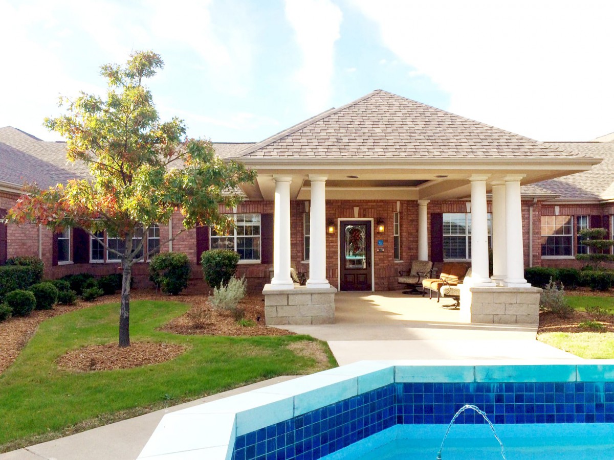 A brick house with a porch and swimming pool in the foreground.