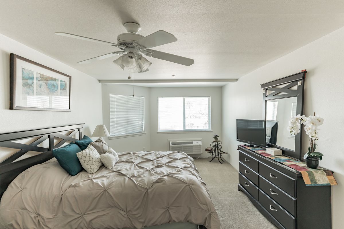 A cozy bedroom with a ceiling fan, bed, dresser, and window letting in natural light.