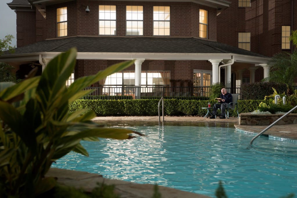 A serene outdoor pool area in front of a building at dusk with a person sitting nearby.