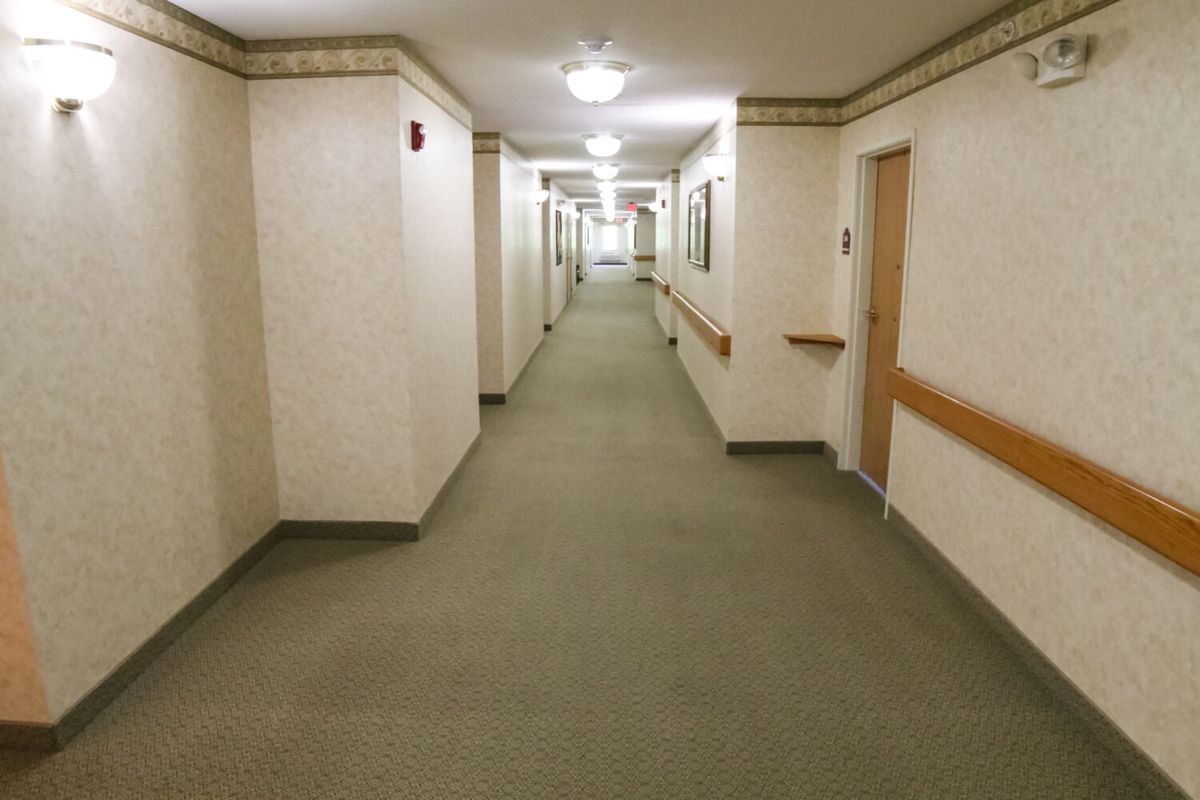 A long, carpeted hallway with multiple doors and ceiling lights.