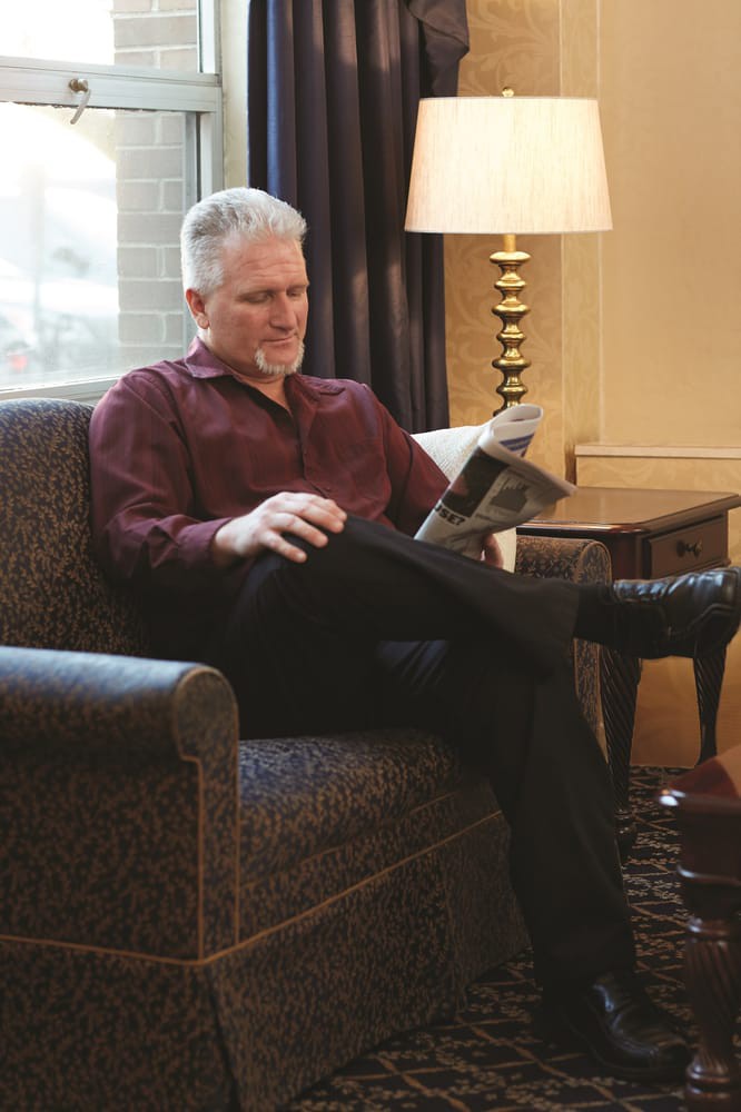 A person relaxing in a chair while reading a newspaper indoors.