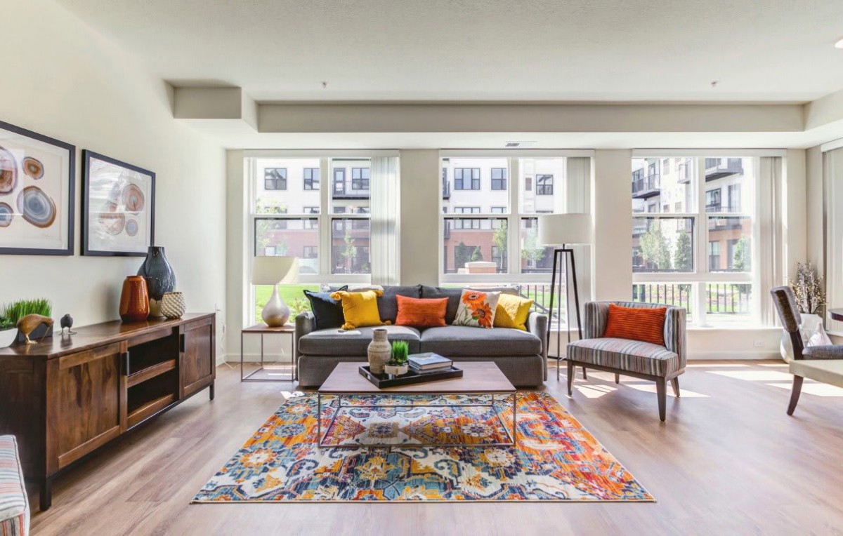 A bright and modern living room with colorful pillows and a patterned rug, featuring large windows that provide ample natural light.