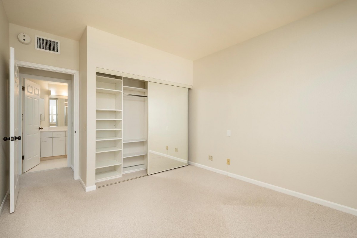 An empty room featuring a closet with mirrored sliding doors and built-in shelves.