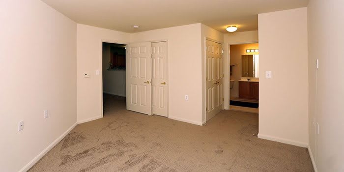 An empty bedroom with carpet flooring, featuring closets and a doorway leading to a bathroom.