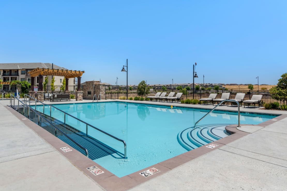 An inviting outdoor swimming pool surrounded by deck chairs under a clear blue sky.