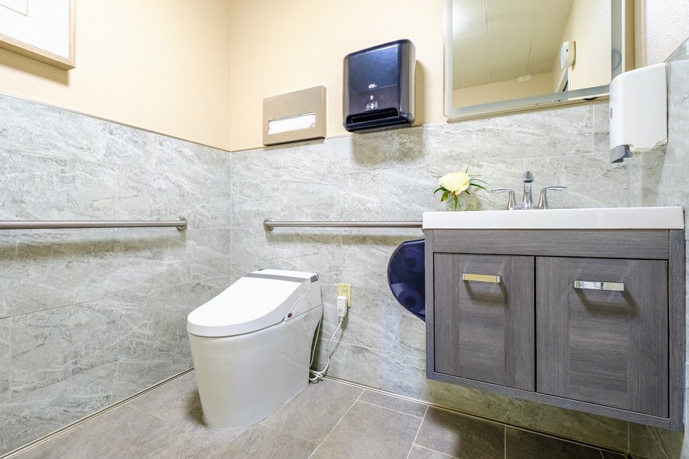 A modern and accessible bathroom featuring a toilet, sink, and safety handrails.